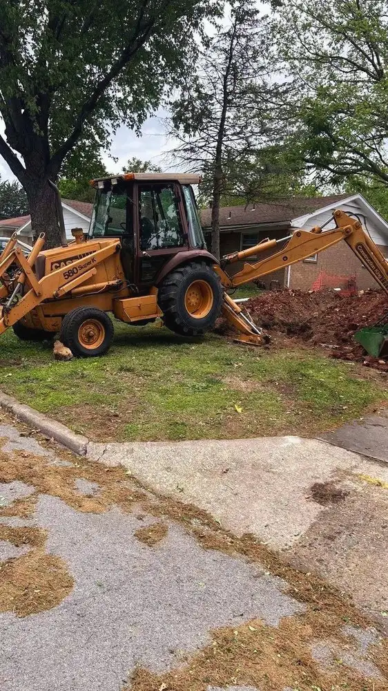 Backhoe excavating a water line beside a house